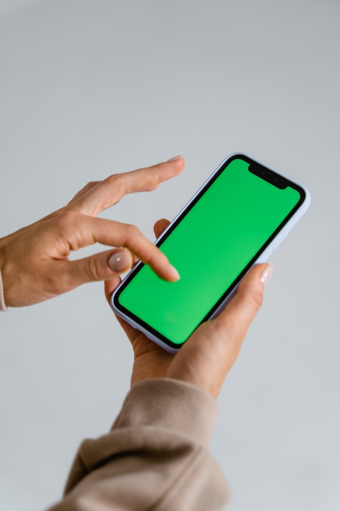 A person interacting with a smartphone displaying a green screen, ideal for design mockups.